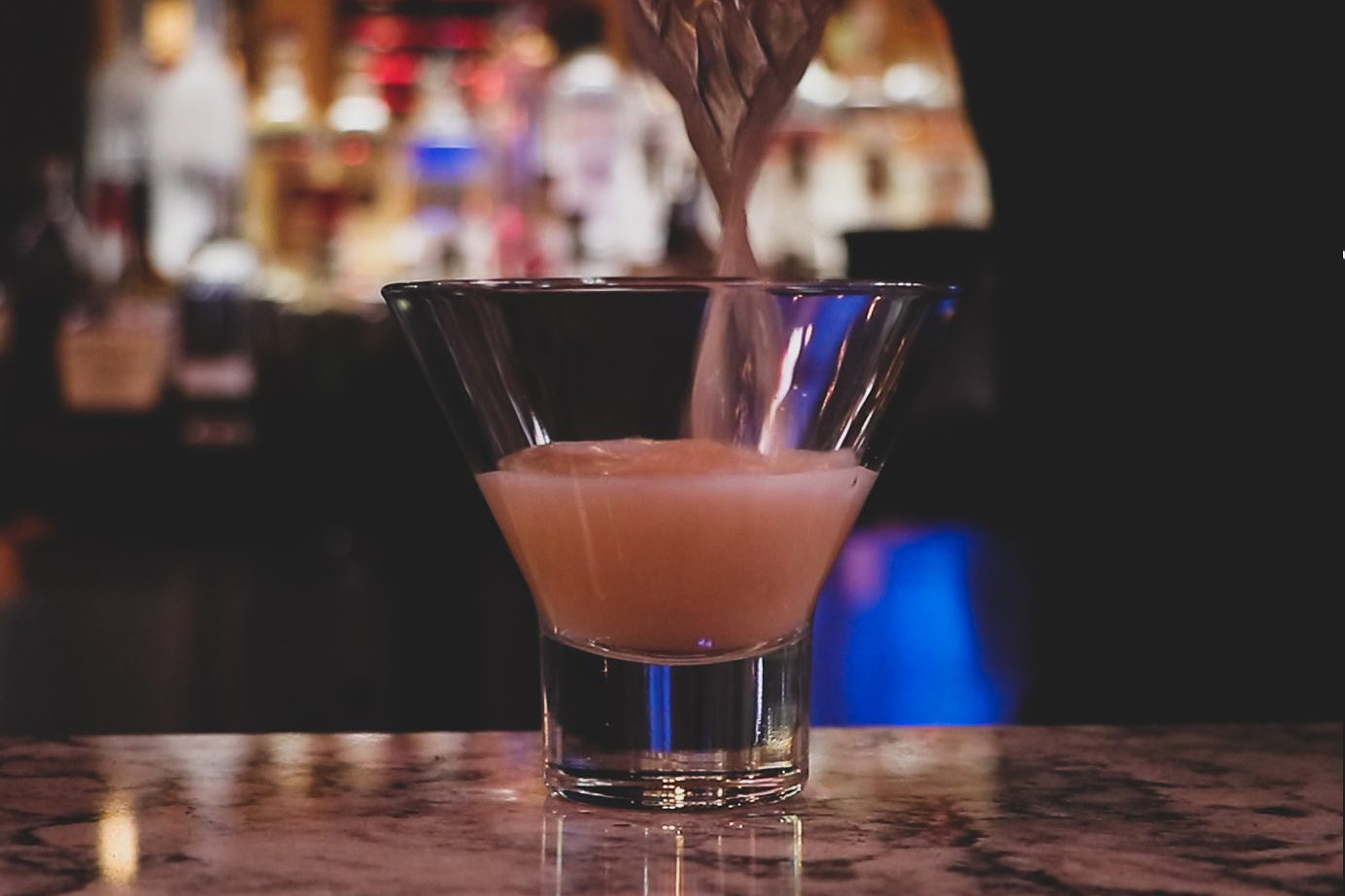 A pink cocktail being poured at the bar